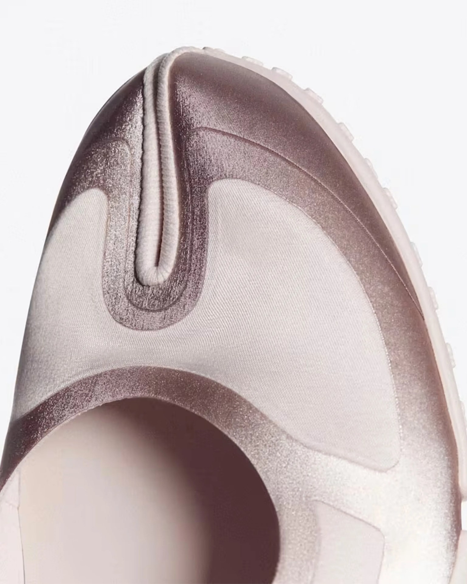 Close-up of a sneaker toe box with a shiny, translucent brown overlay and light beige fabric underneath.
