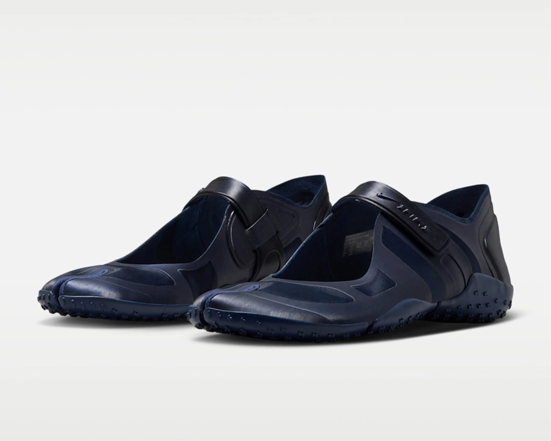 Pair of navy blue minimalist slip-on shoes with textured soles and adjustable straps.