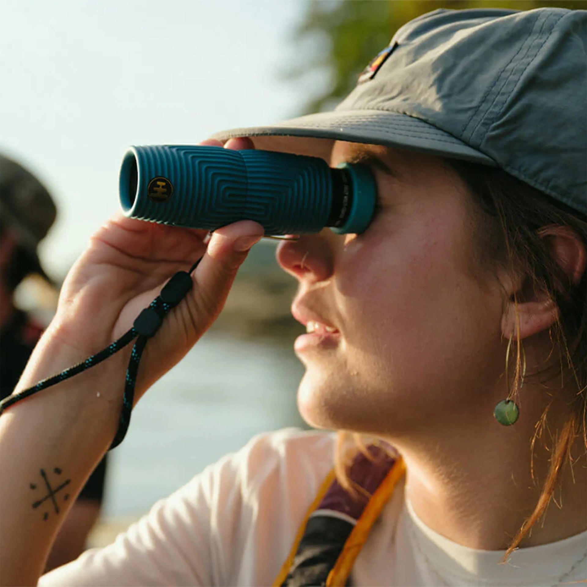 Person wearing a gray cap looking through a blue monocular with a wrist strap.