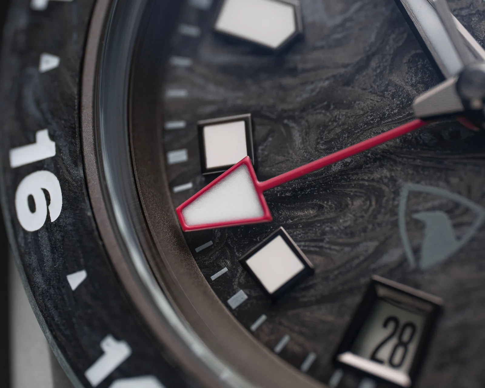 Close-up of a watch face showing a red-tipped arrow hand, square hour markers, and a date window displaying "28".