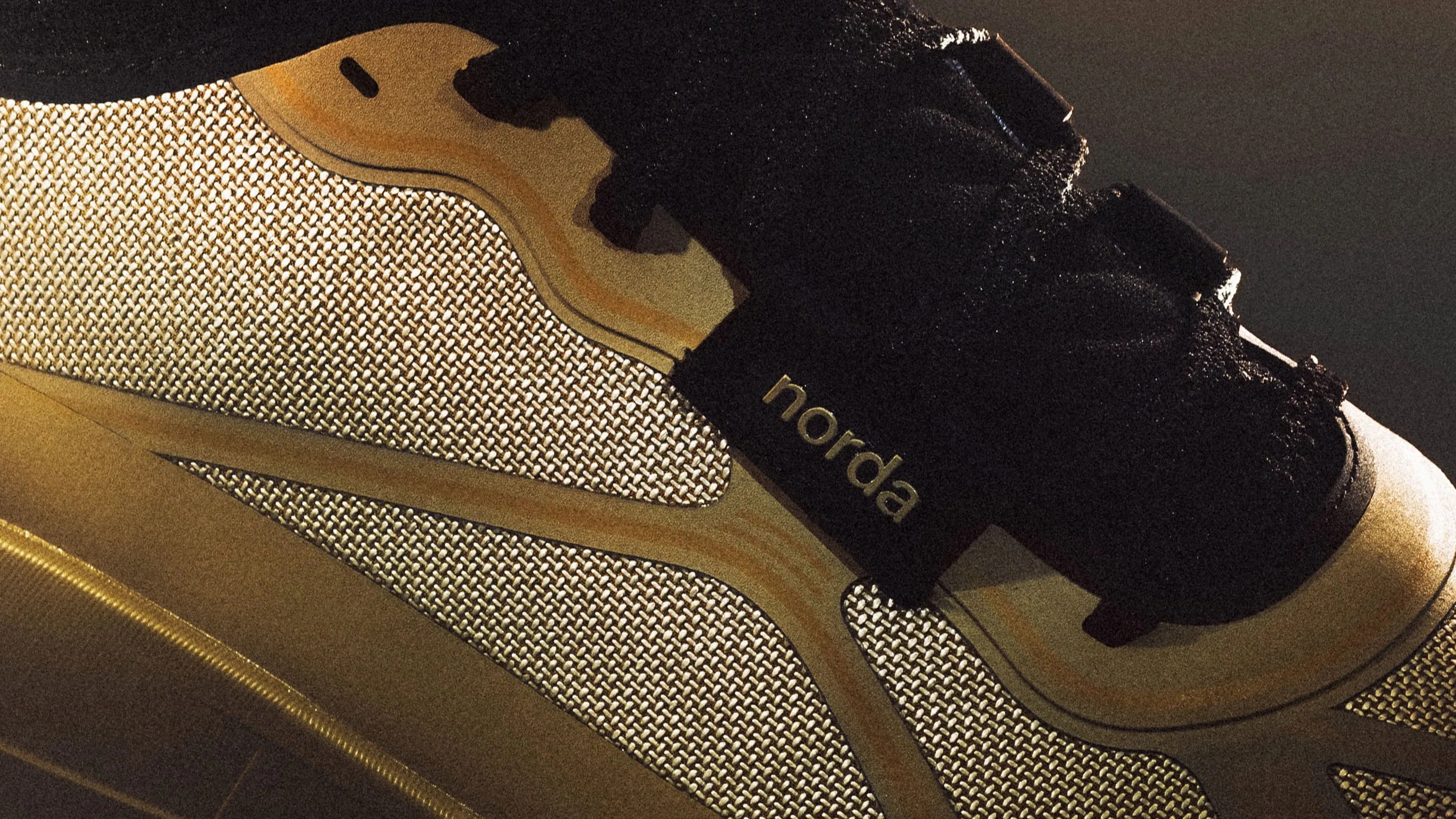 Close-up of a beige and black sneaker with woven fabric and "norda" branding on the side.