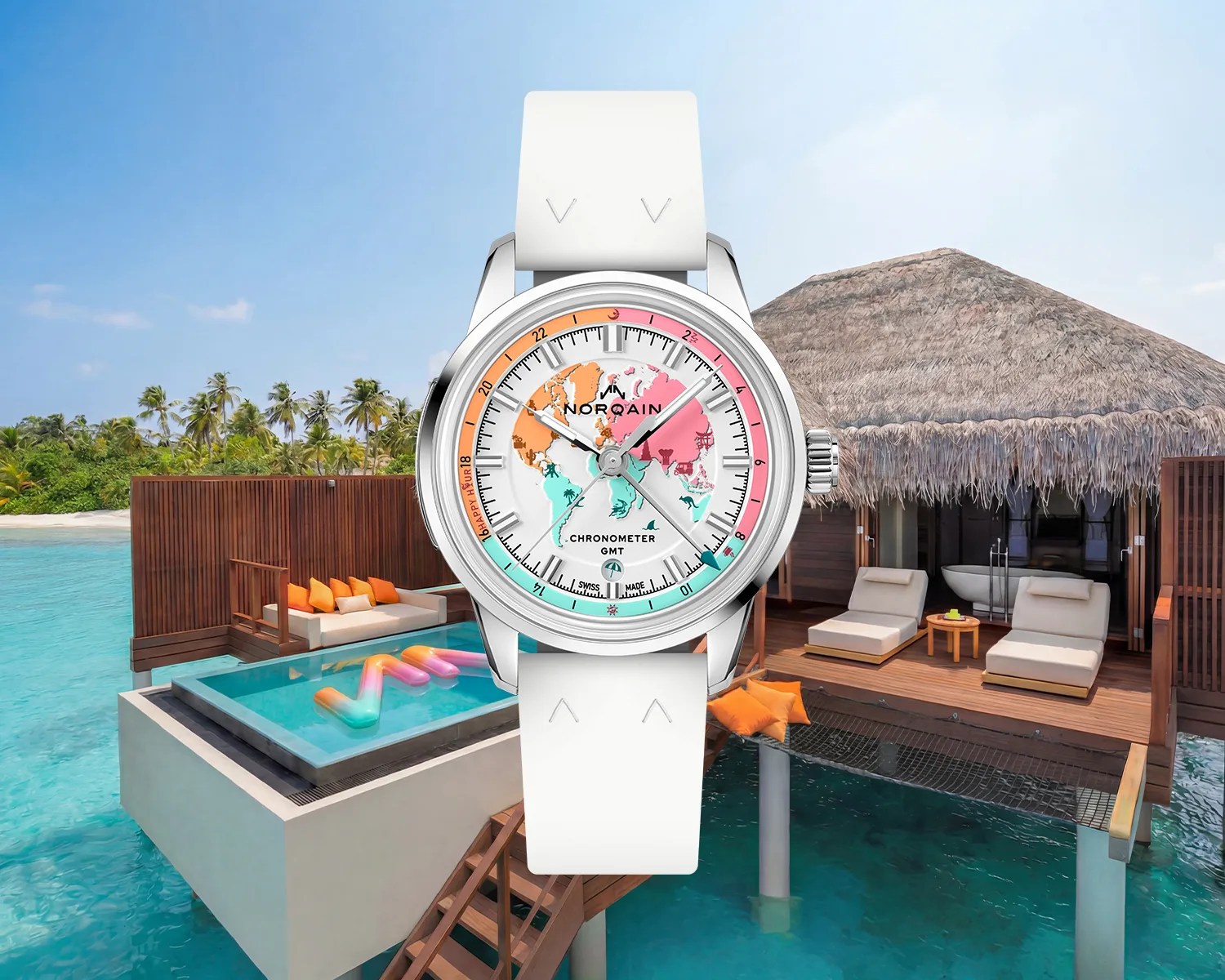 Silver Norqain chronometer GMT watch with a colorful world map dial and white strap over a tropical overwater bungalow background.