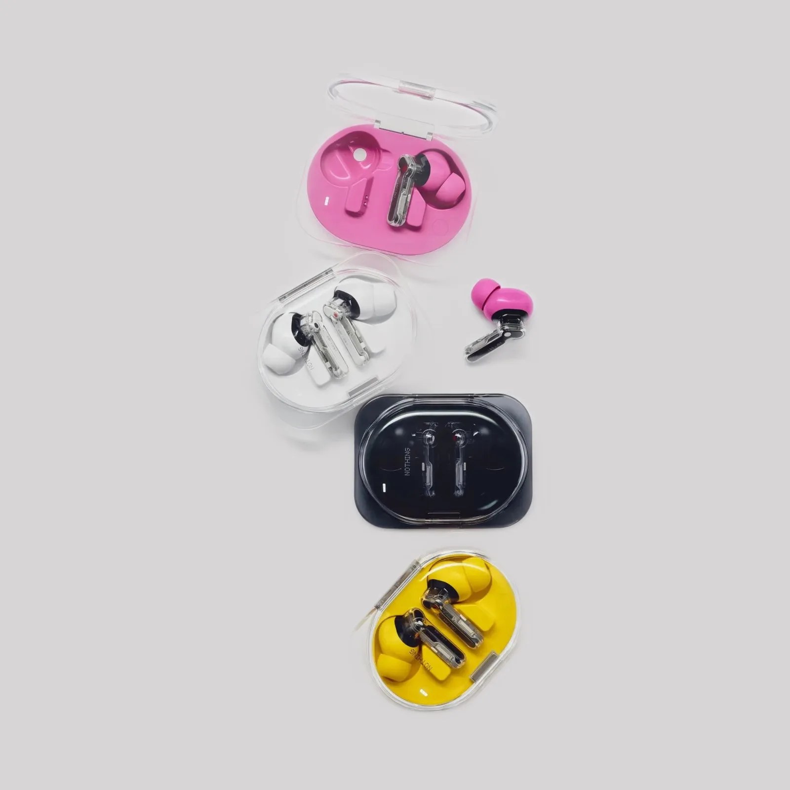 Four pairs of wireless earbuds in transparent cases with pink, white, black, and yellow interiors on a light gray background.