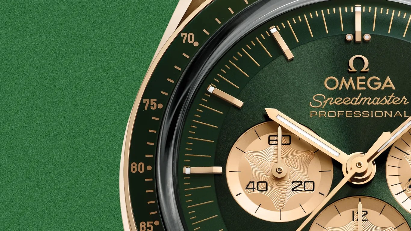 Close-up of an Omega Speedmaster Professional watch face with green dial and gold subdials and hands.