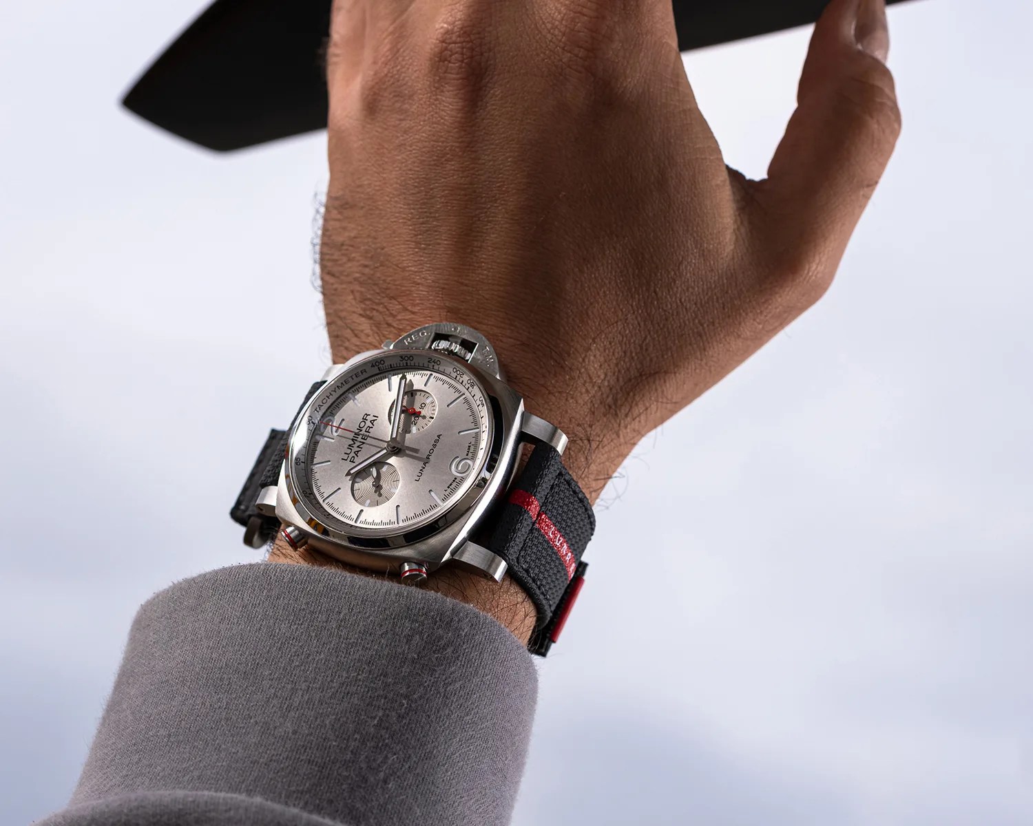 Silver Panerai Luminor Luna Rossa watch with black fabric strap featuring a red stripe, worn on a wrist.