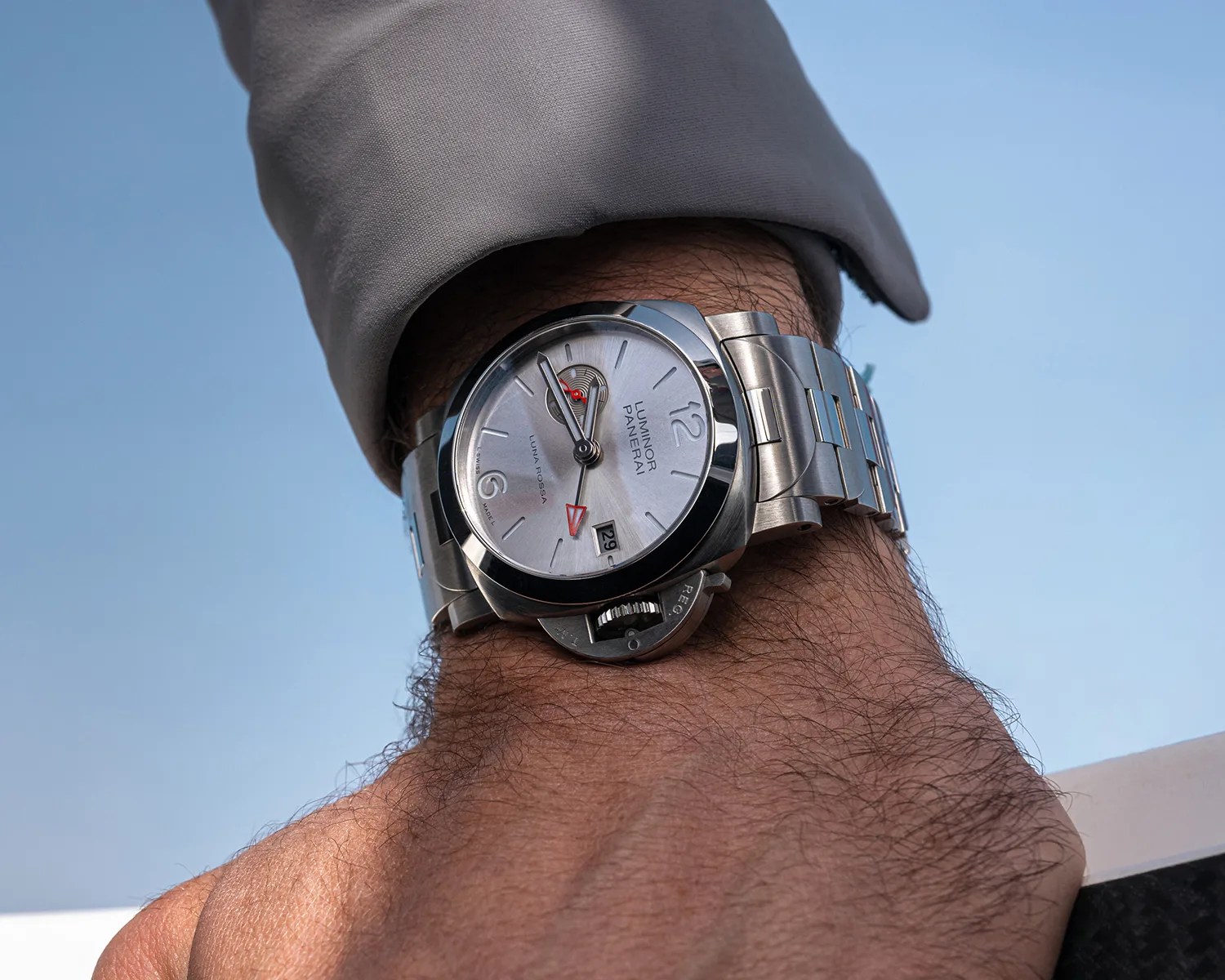 Silver Panerai Luminor wristwatch with metal bracelet and white dial worn on a wrist.