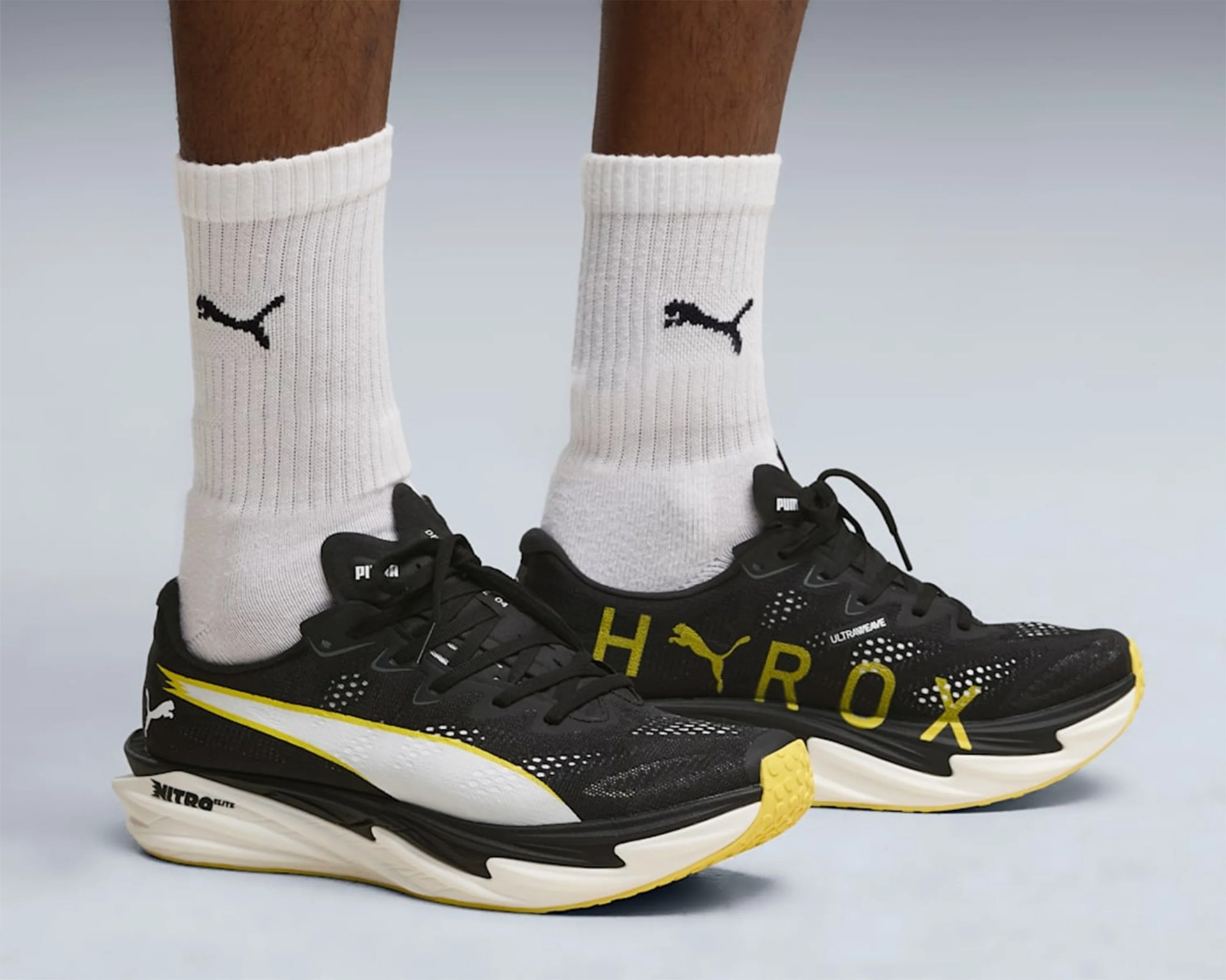 Black and yellow Puma running shoes with white Puma logo and white socks with black Puma logo.