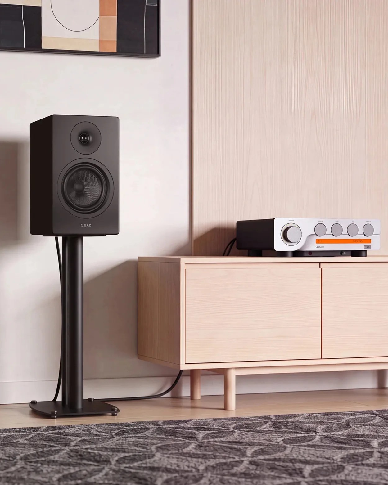 Black Quad speaker on a stand next to a light wood cabinet with a silver Quad amplifier on top.