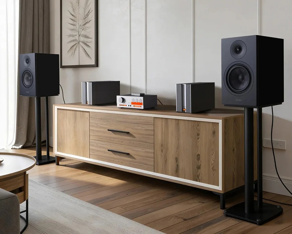 Pair of black bookshelf speakers on stands flanking a wooden media console with audio equipment on top.