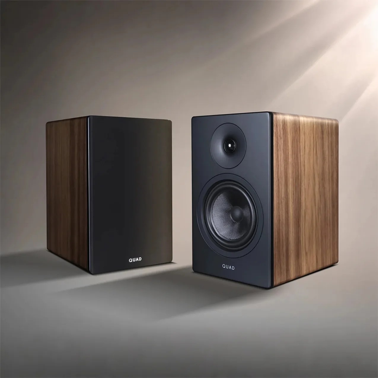 Pair of rectangular wooden bookshelf speakers with black front panels, one showing drivers and the other covered, labeled "QUAD.