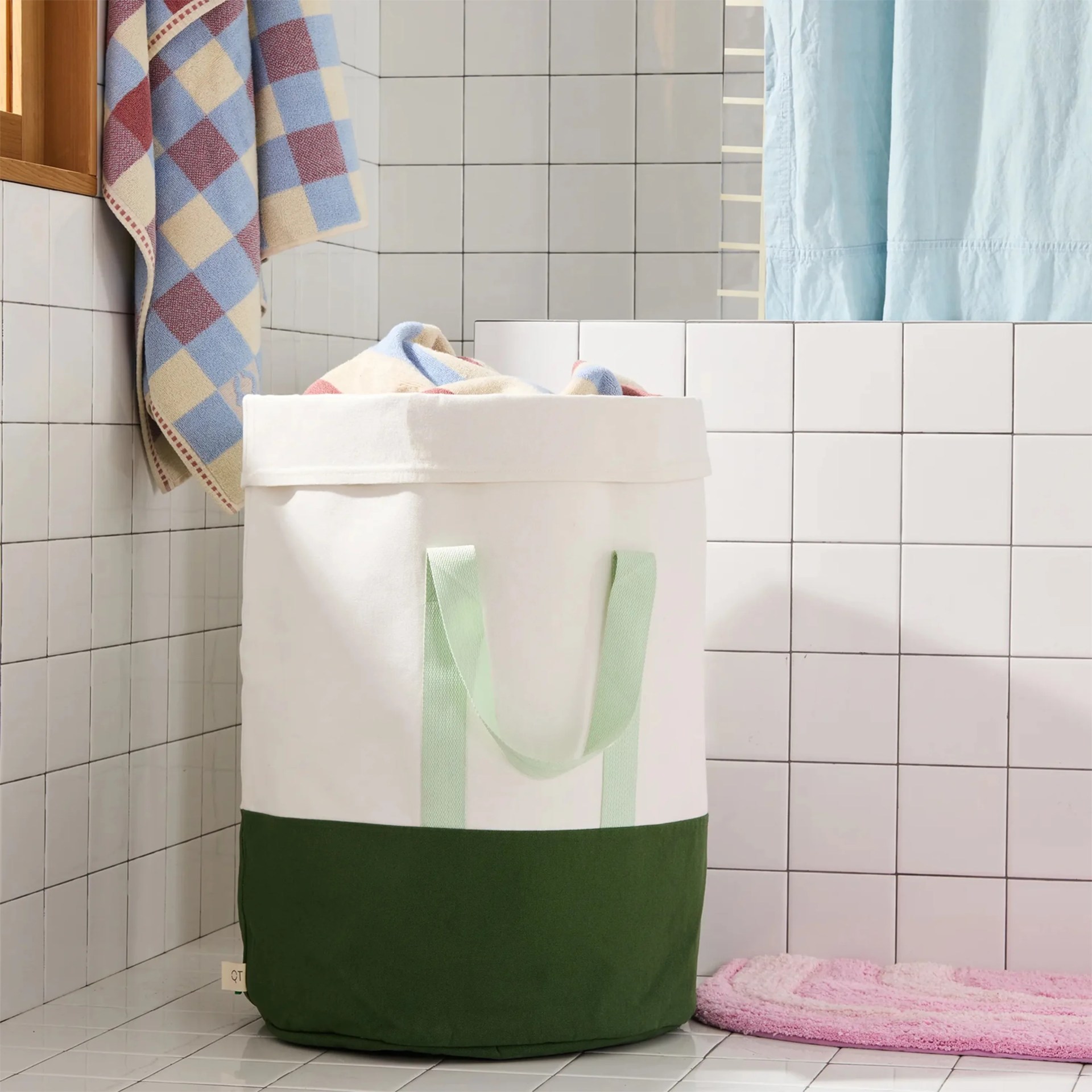 White and dark green fabric laundry basket with light green handles in a tiled bathroom corner.
