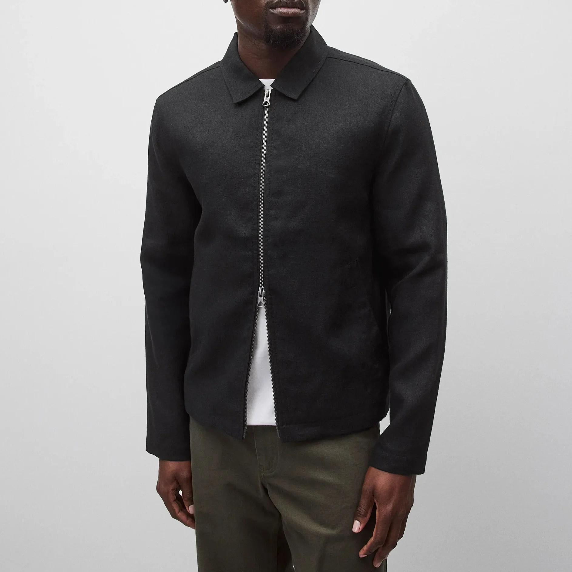 Black zip-up jacket with a collar worn over a white shirt and paired with olive green pants.