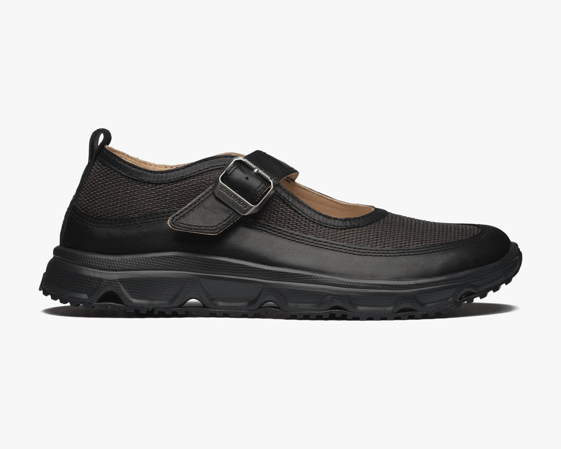 Black Mary Jane shoe with textured mesh upper, leather strap with metal buckle, and thick rubber sole.