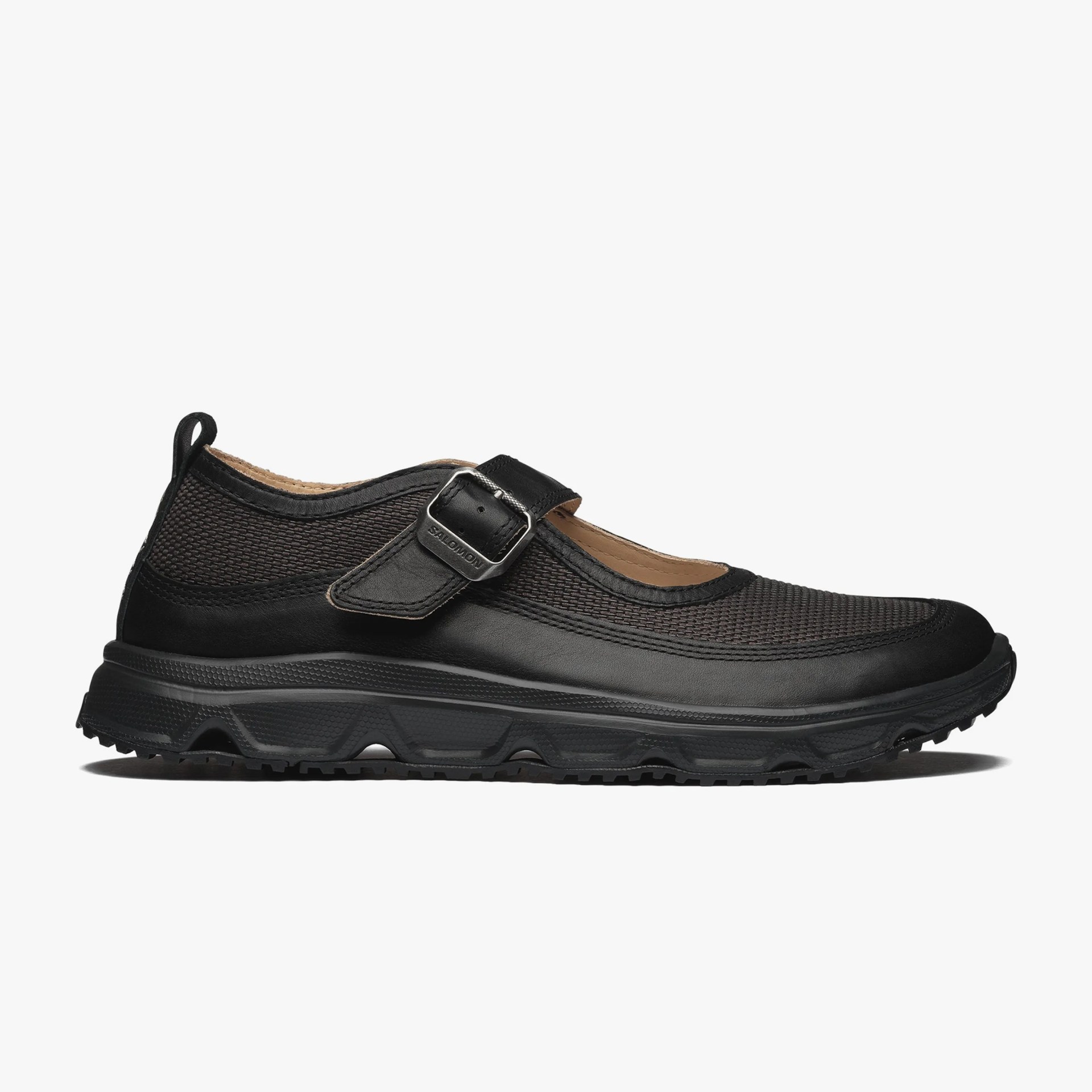 Black Mary Jane shoe with textured fabric upper, leather strap with metal buckle, and rugged sole.