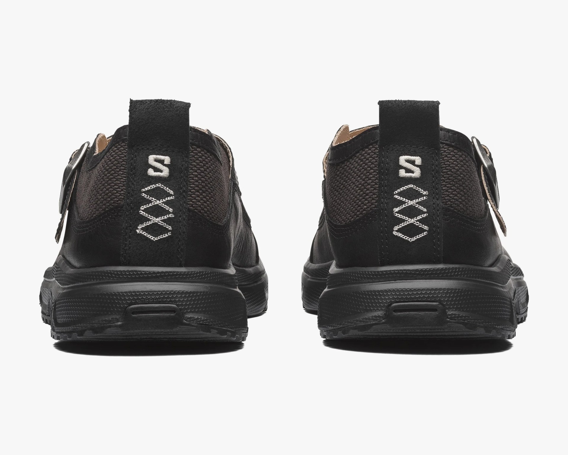 Pair of black shoes with textured fabric and leather back panels, featuring white stitched "S" and diamond patterns on heel tabs.