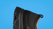Black textured athletic shoe with thick sole and pull tab on a blue background.