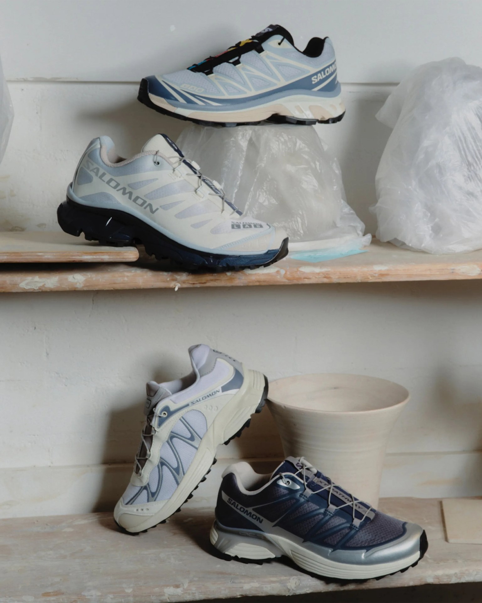 Four pairs of Salomon running shoes in various shades of blue and white displayed on wooden shelves.
