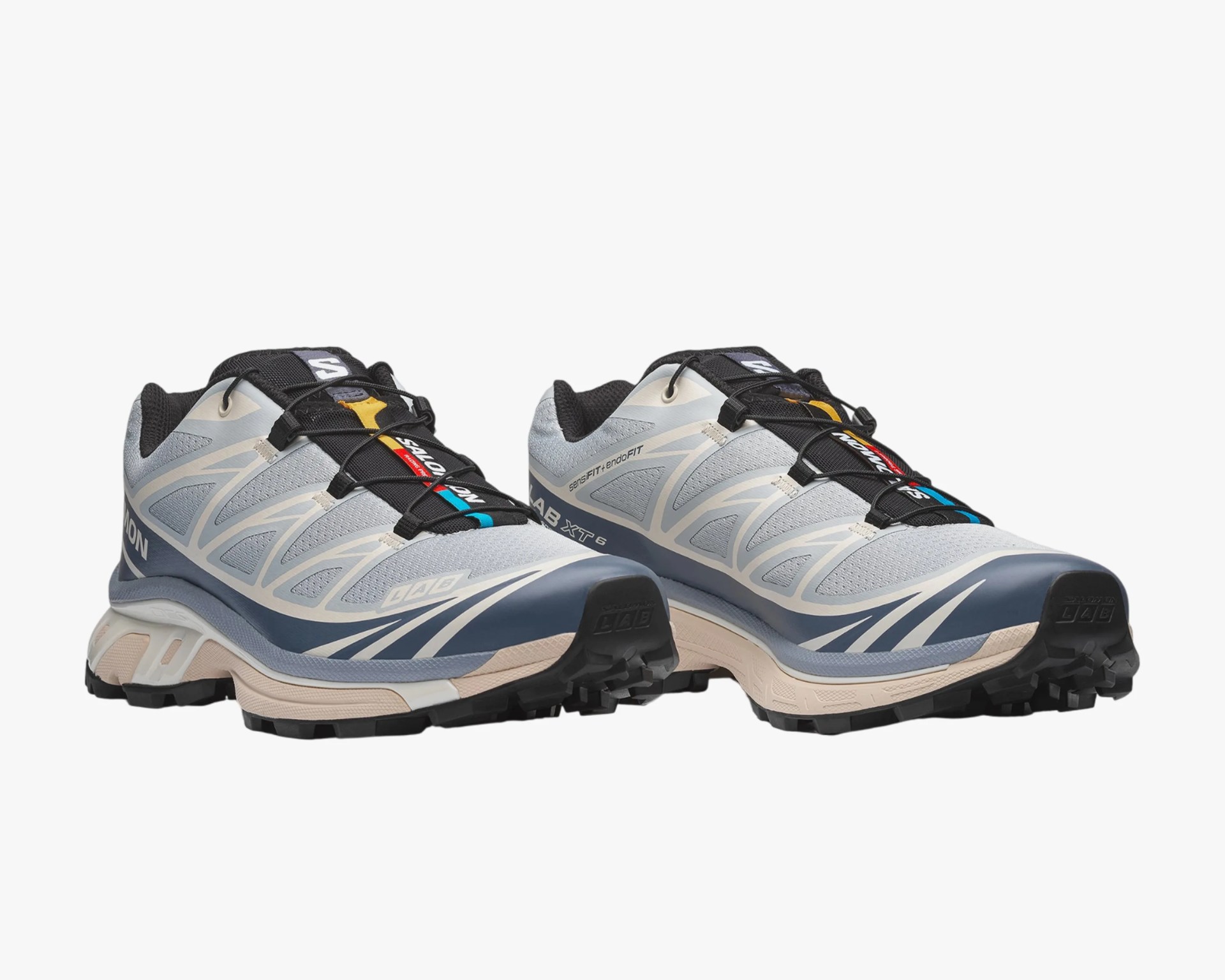 Light gray and navy trail running shoes with black laces and rugged beige soles.