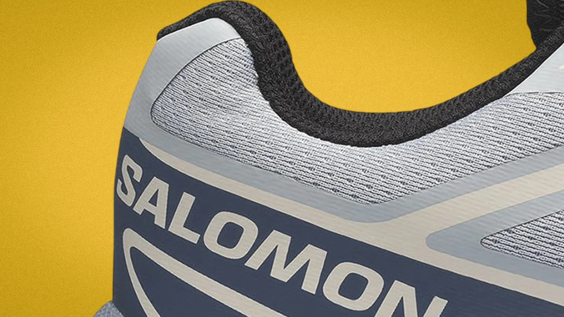Close-up of the heel area of a gray and navy Salomon shoe with black inner lining against a yellow background.