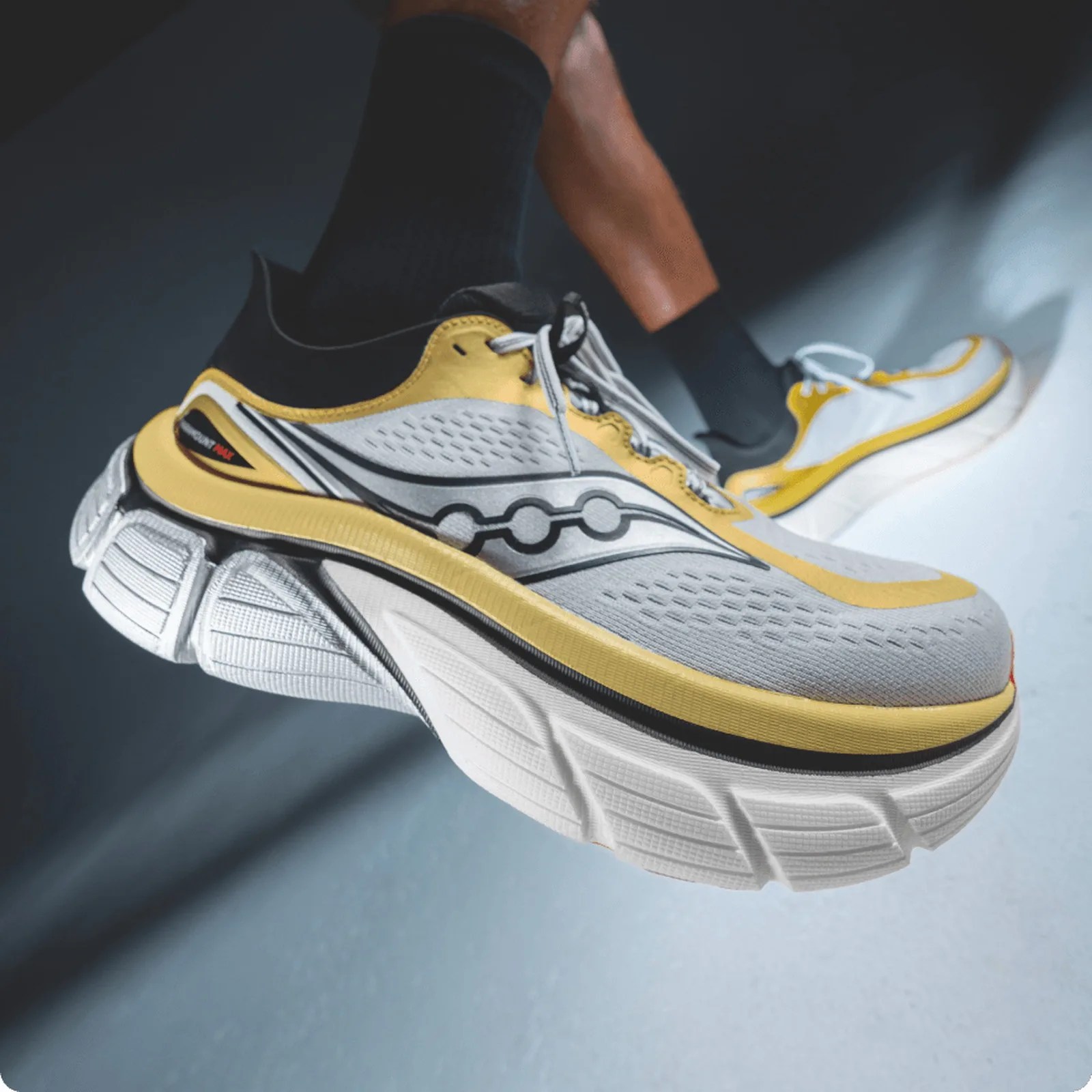 White and yellow Saucony running shoes with thick soles worn with black socks.