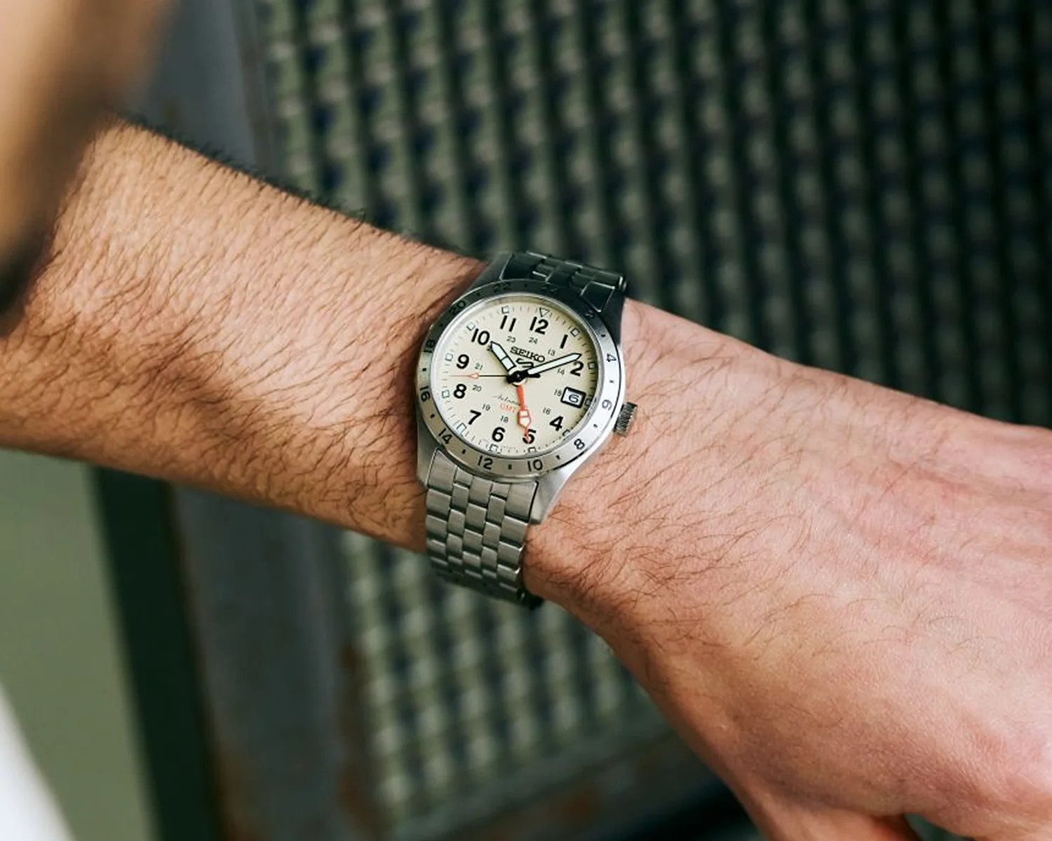 Silver Seiko wristwatch with cream dial and metal link band worn on a wrist.