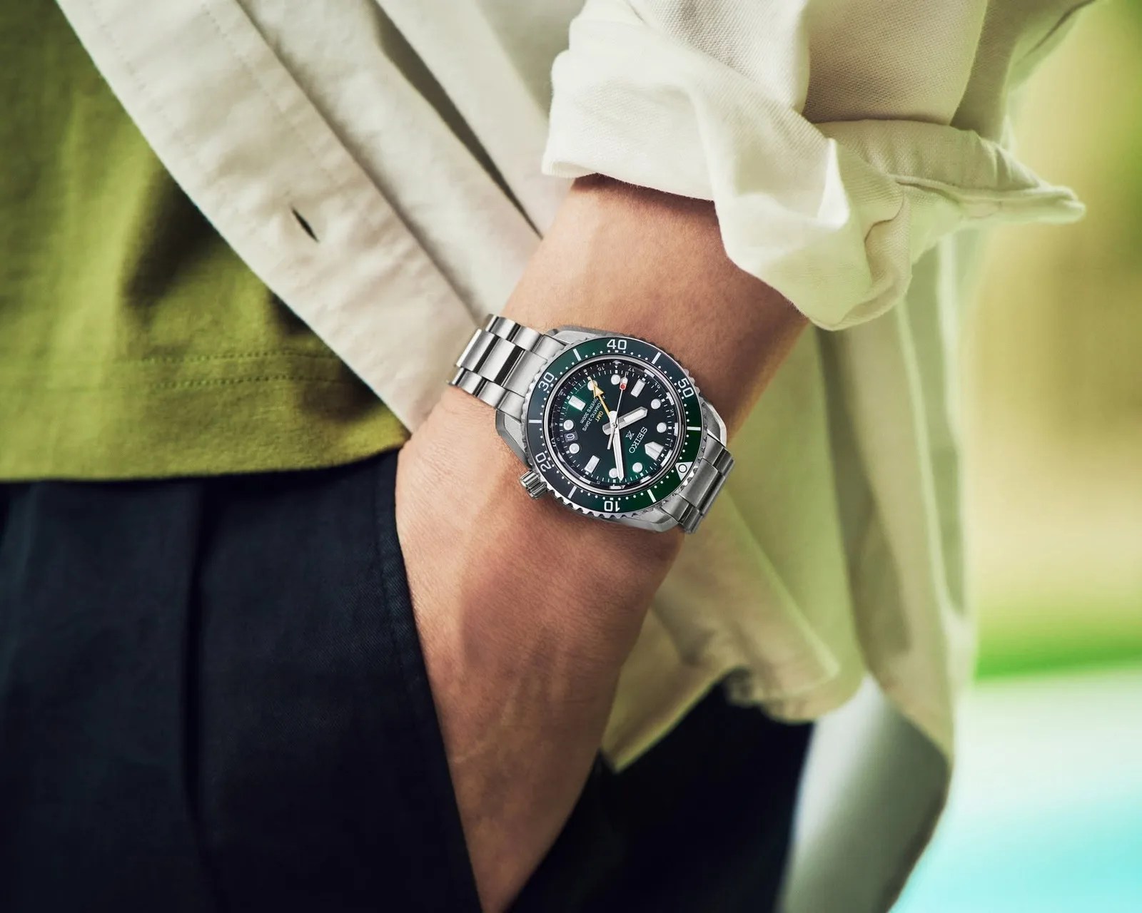 Silver metal Seiko dive watch with green and black bezel worn on a wrist with a rolled-up white shirt sleeve.