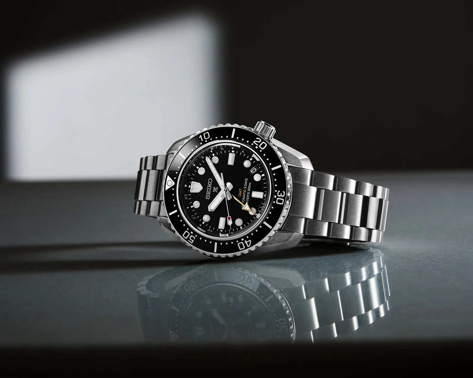 Stainless steel Seiko diver's watch with black dial, rotating bezel, and metal bracelet on reflective surface.
