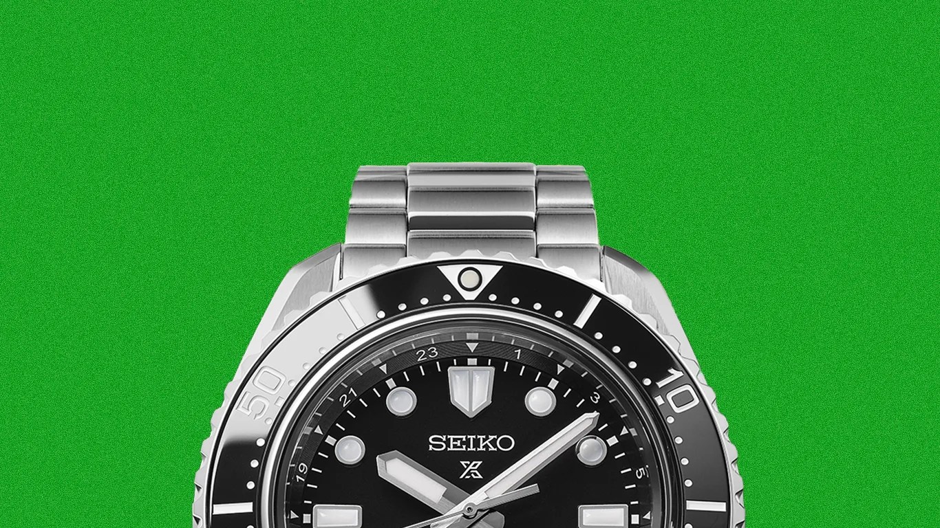 Silver Seiko dive watch with black bezel and black dial on a green background.