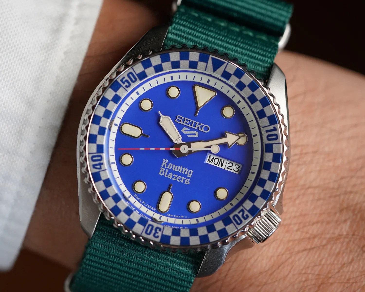 Seiko wristwatch with blue dial, white and blue checkered bezel, luminous markers, and green fabric strap.