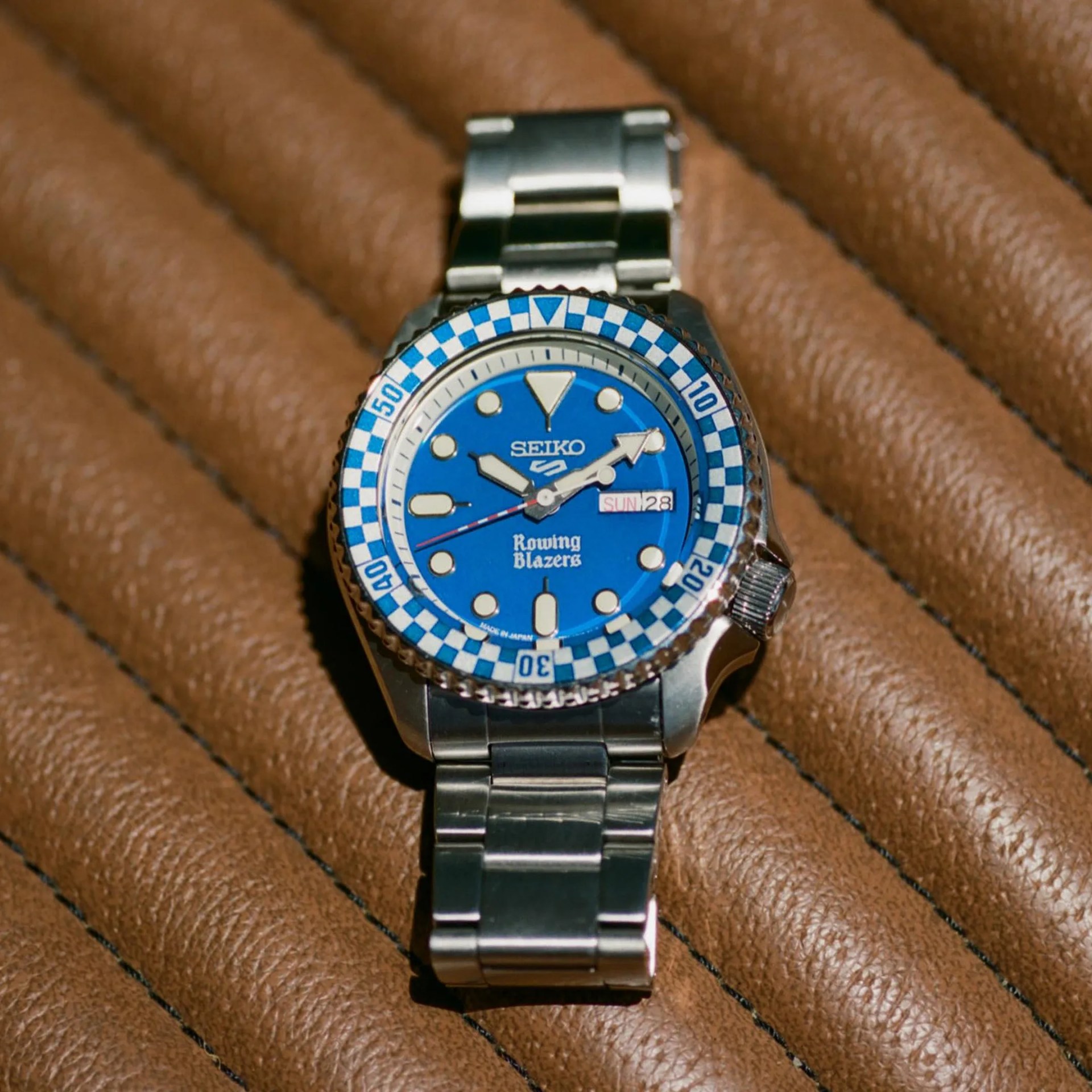 Seiko wristwatch with blue dial, checkered bezel, and stainless steel bracelet on a brown textured surface.