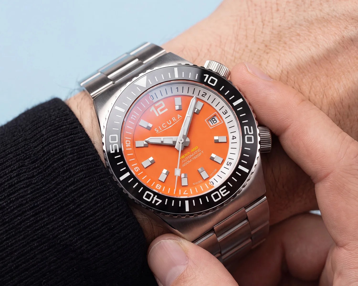 Stainless steel Sicura wristwatch with bright orange dial and black rotating bezel worn on a wrist.
