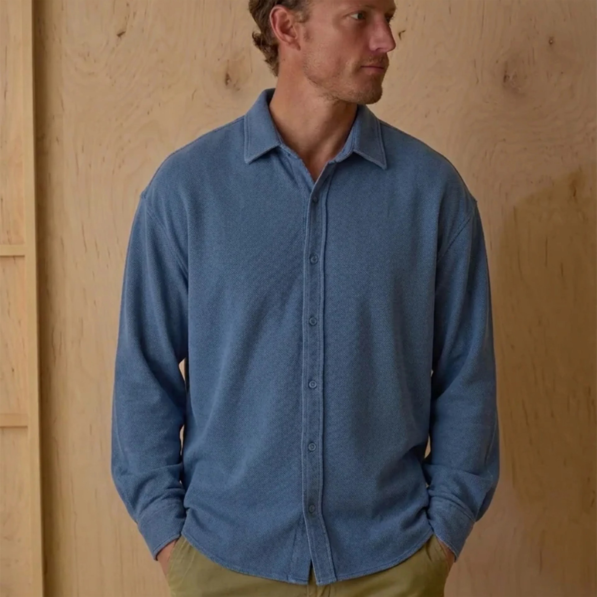 Blue long-sleeve button-up shirt worn by a person with hands in olive-green pants pockets.