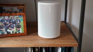 White Sonos wireless speaker on a wooden shelf next to a framed photo.