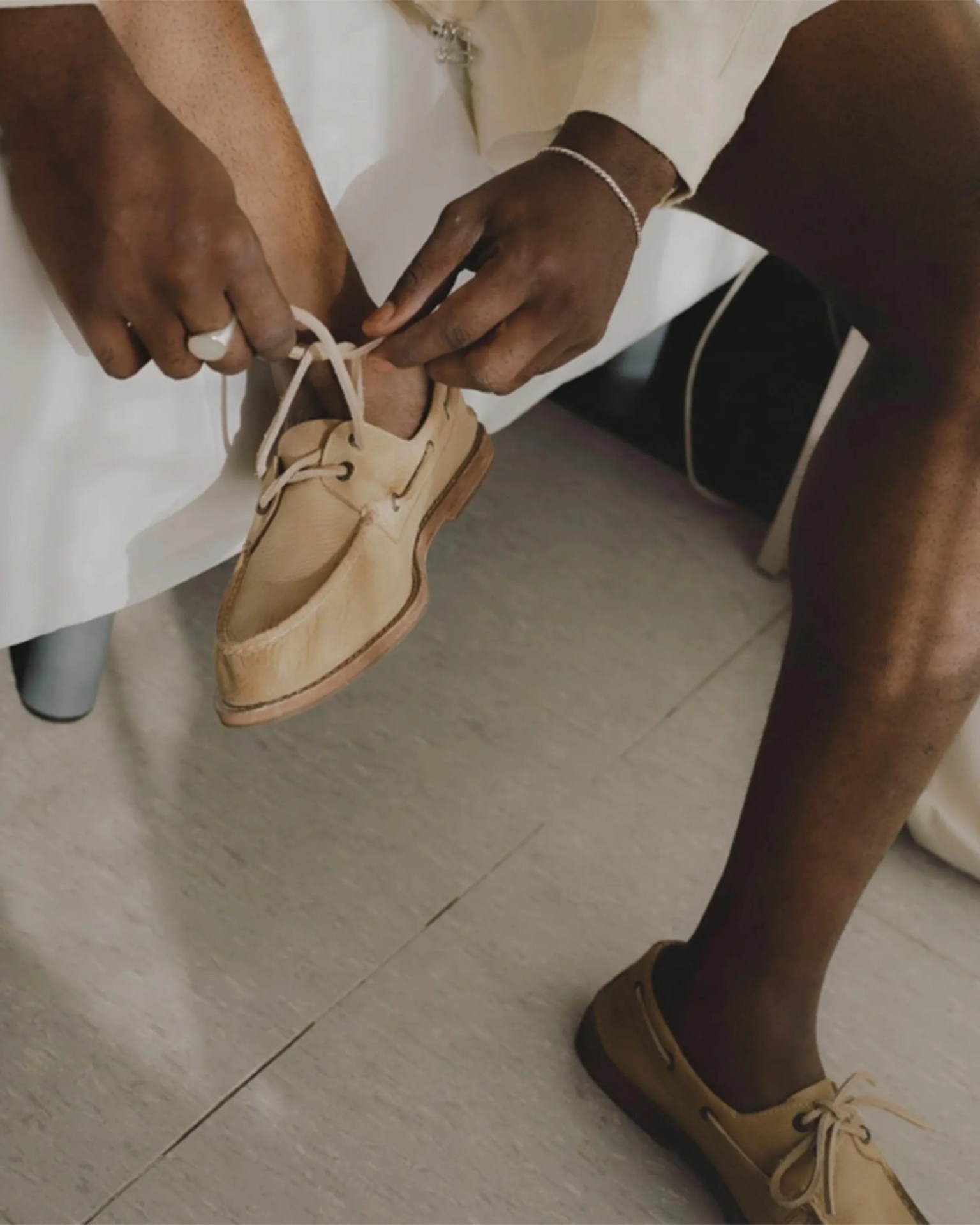 Hands tying laces on tan leather boat shoes worn with white pants.