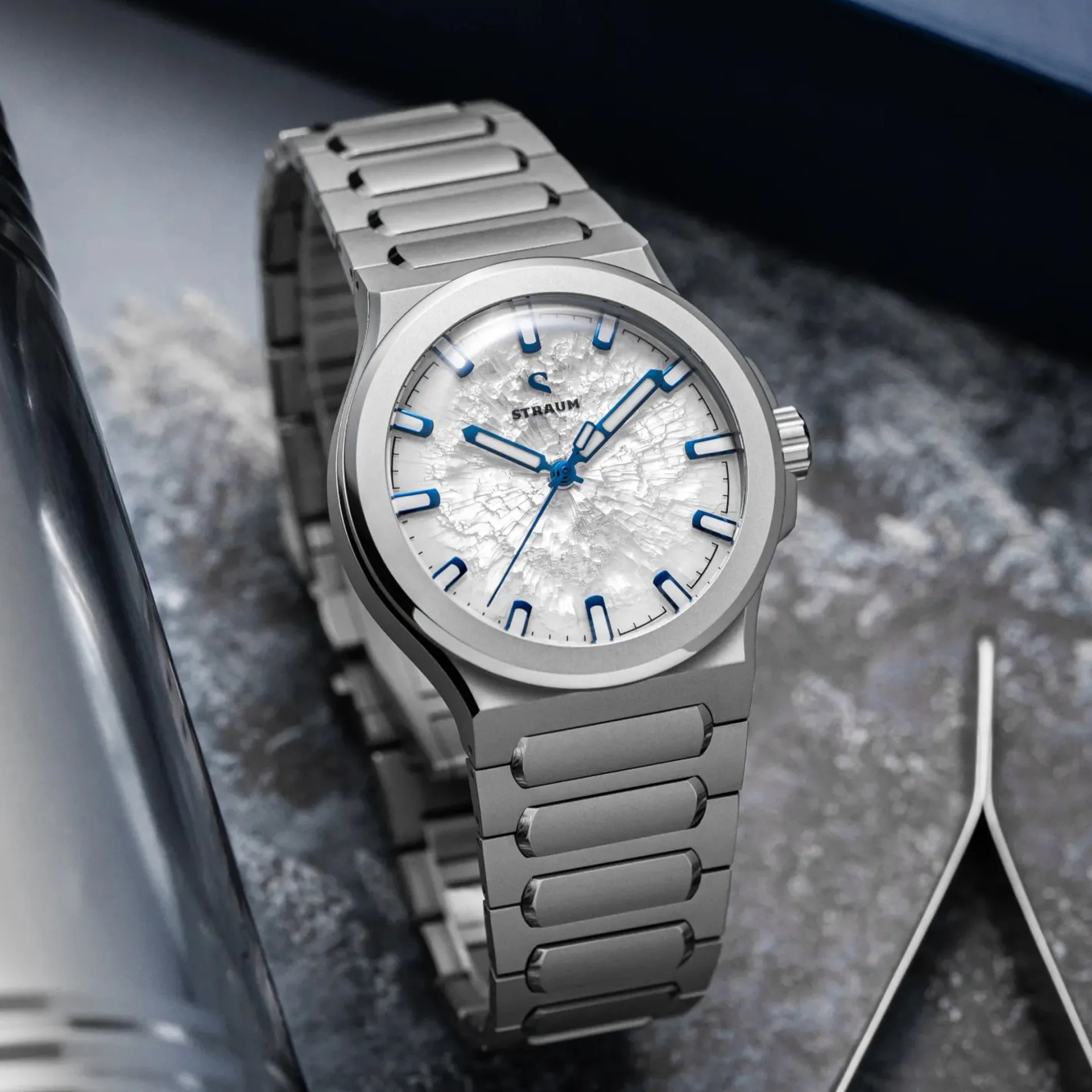 Silver metal wristwatch with blue hour markers and hands on a textured white dial.