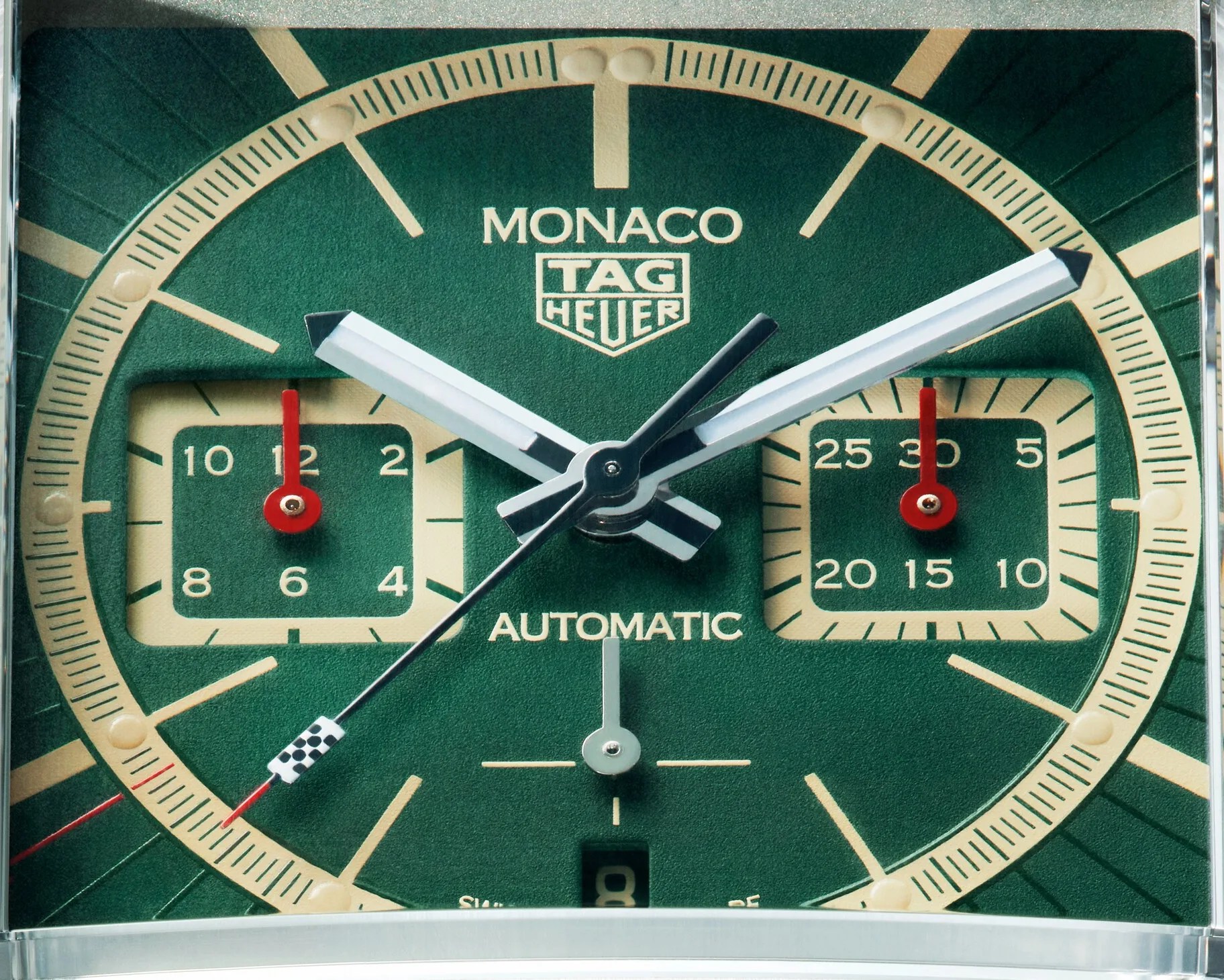 Close-up of a green TAG Heuer Monaco automatic watch face with cream accents and red hands on subdials.