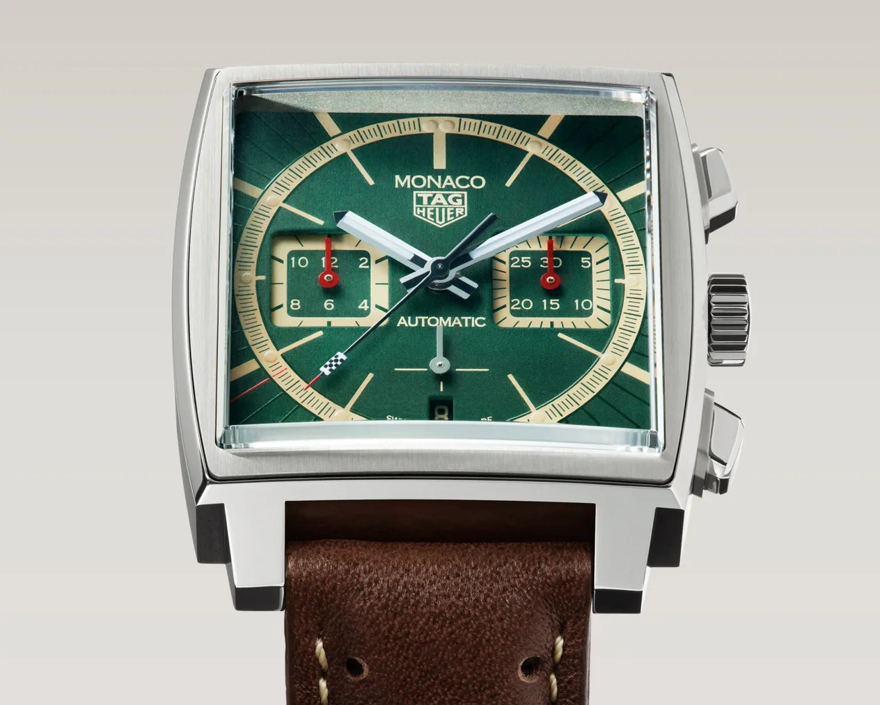 Square silver TAG Heuer Monaco watch with green dial, beige subdials, and brown leather strap.