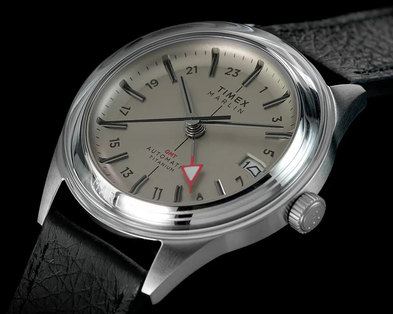 Close-up of a Timex Marlin automatic titanium watch with a beige dial, black leather strap, and red GMT hand.