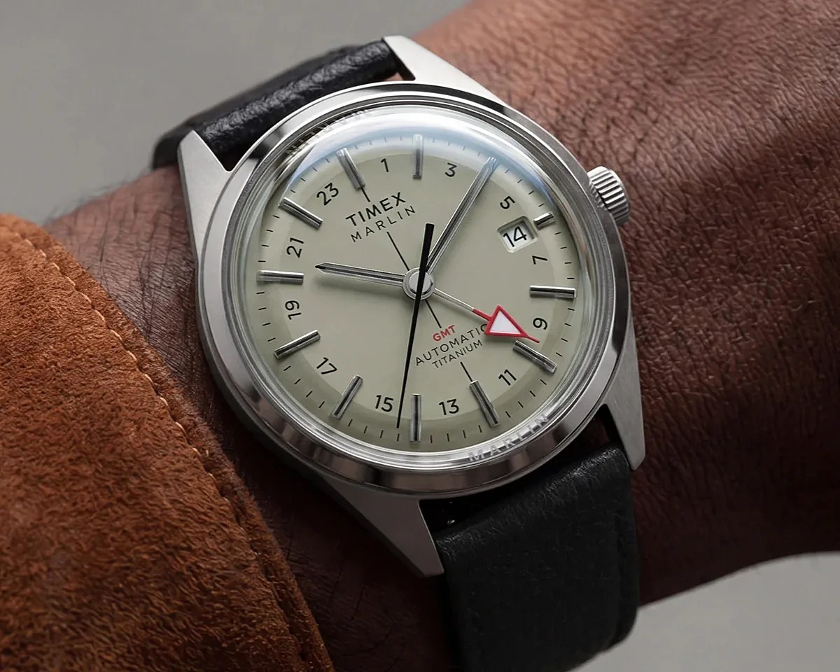 Timex Marlin GMT automatic titanium watch with cream dial and black leather strap on a wrist.