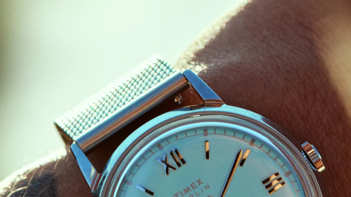 Close-up of a Timex wristwatch with a silver mesh band on a wrist.