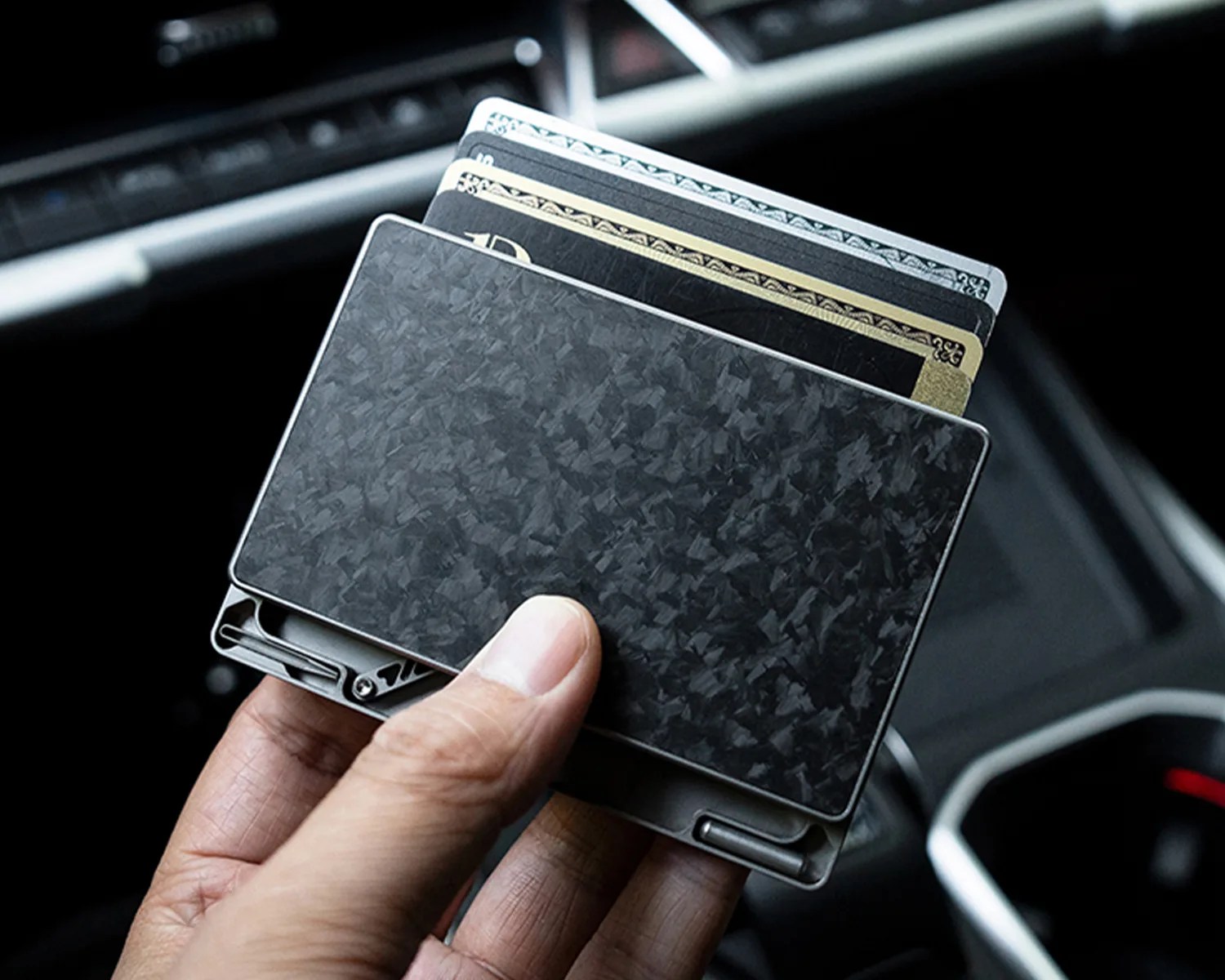 Hand holding a slim, black carbon fiber wallet with several cards partially visible inside.