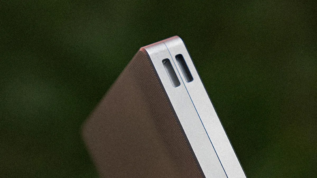 Close-up of a silver laptop corner showing two speaker grilles on a dark blurred background.