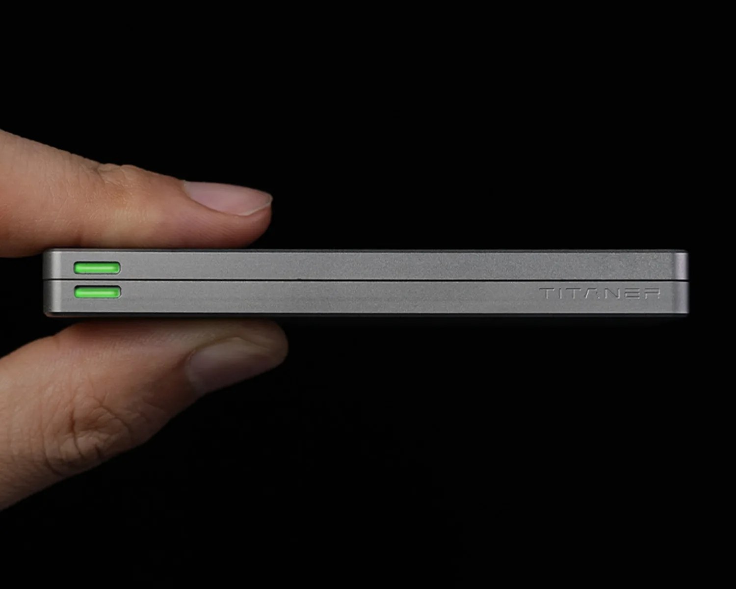 Hand holding a slim, rectangular gray device with two green indicator lights and "TITANER" engraved on the side.