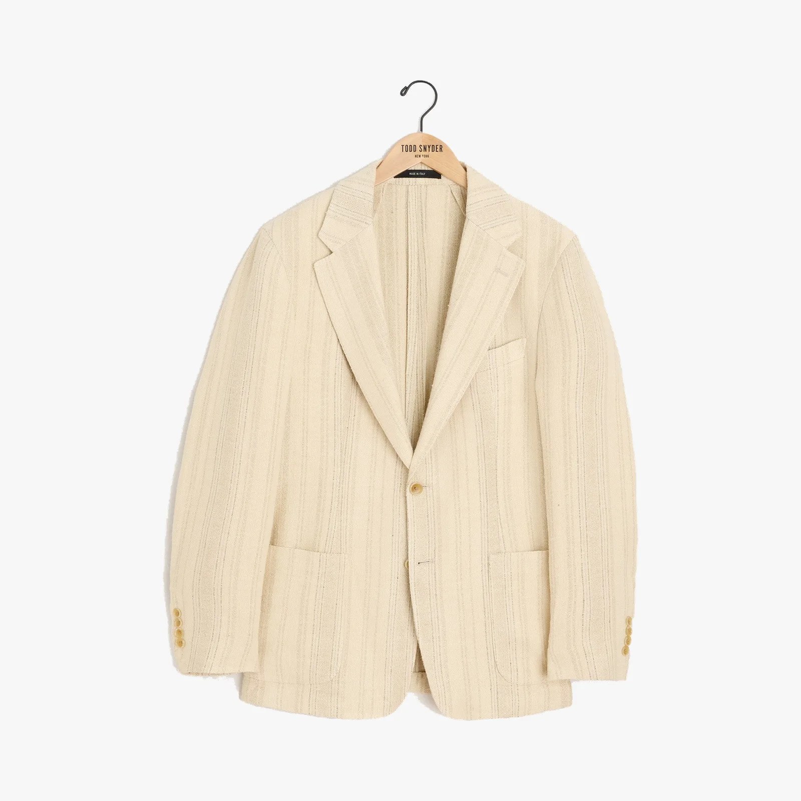Cream-colored textured blazer with notch lapels and two front pockets on a wooden hanger.