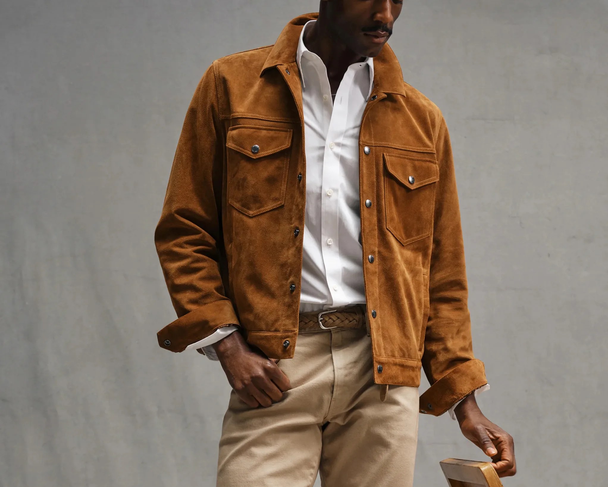 Brown suede jacket with snap buttons and flap pockets worn over a white button-up shirt and beige pants.