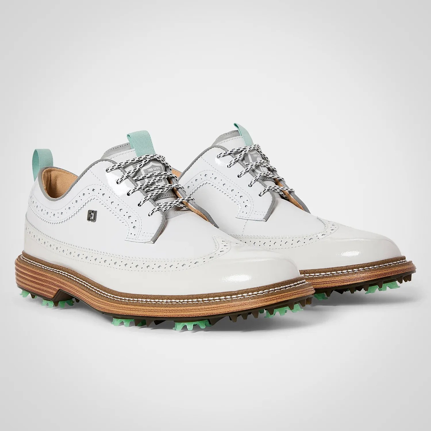 Pair of white leather golf shoes with brogue detailing, wooden midsoles, and green cleated outsoles.