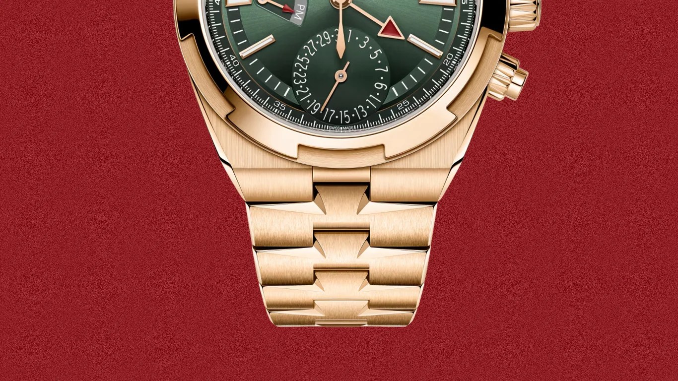 Close-up of a gold metal watch bracelet with a green dial and GMT features on a red textured background.