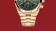 Close-up of a gold metal watch bracelet with a green dial and GMT features on a red textured background.