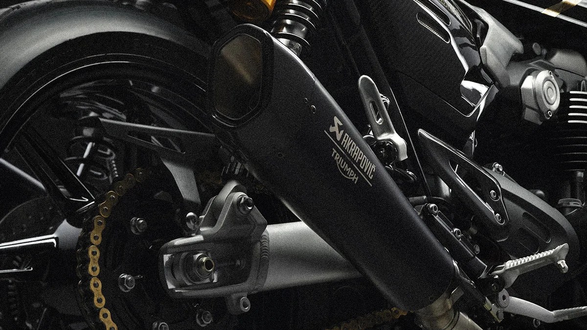 Close-up of a black Akrapovic exhaust pipe on a Triumph motorcycle showing the rear wheel and chain.