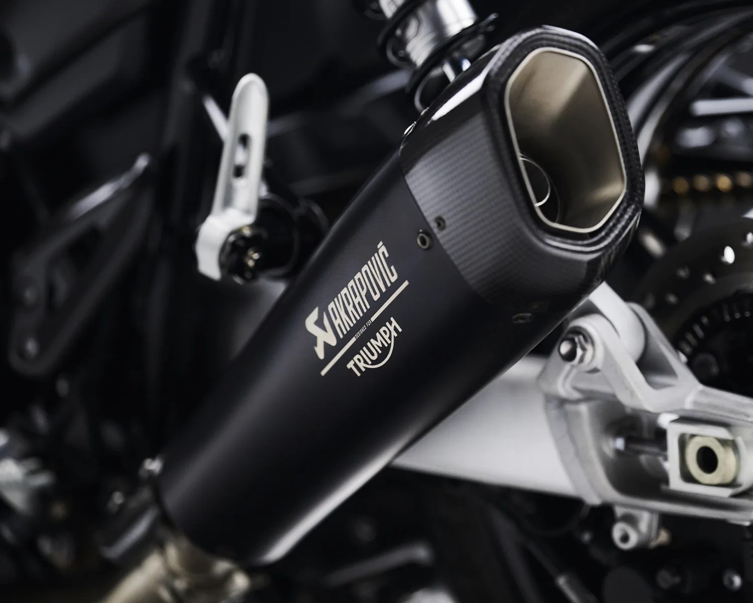 Black Akrapovič exhaust pipe with carbon fiber tip mounted on a Triumph motorcycle.